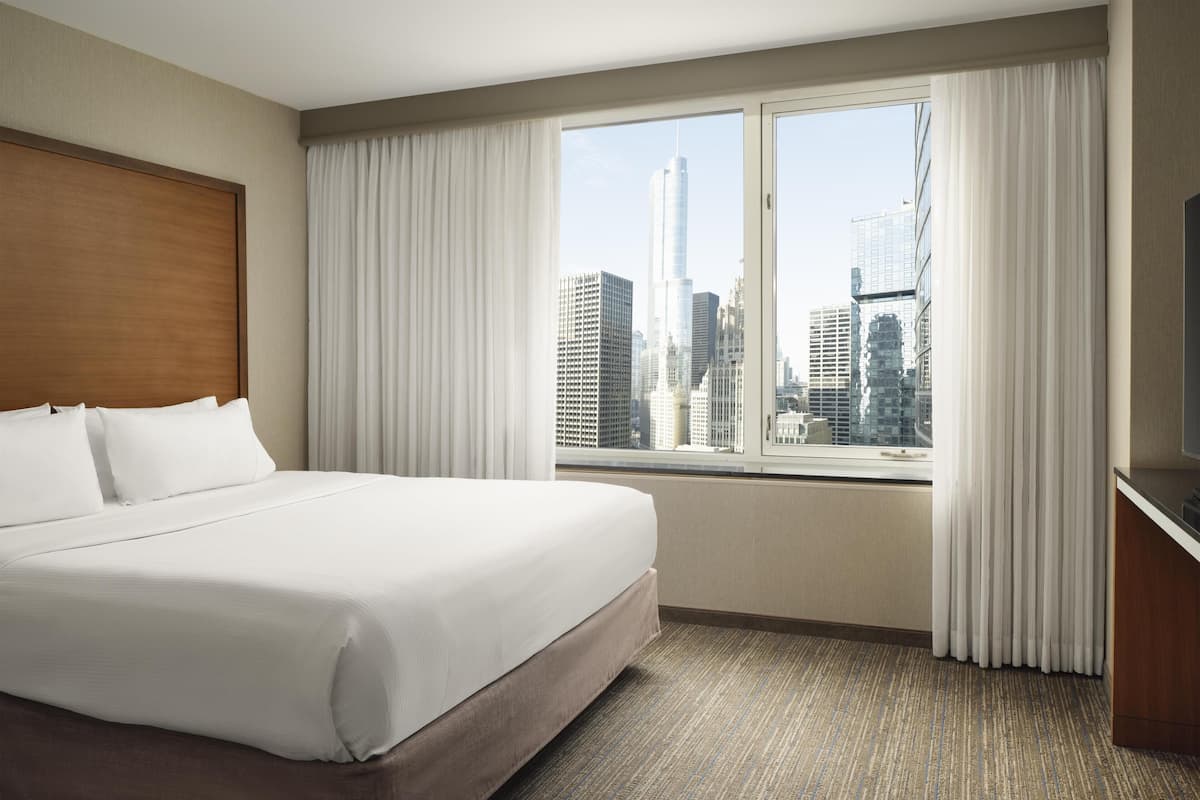 A hotel room with a large bed, a city view, and a television.
