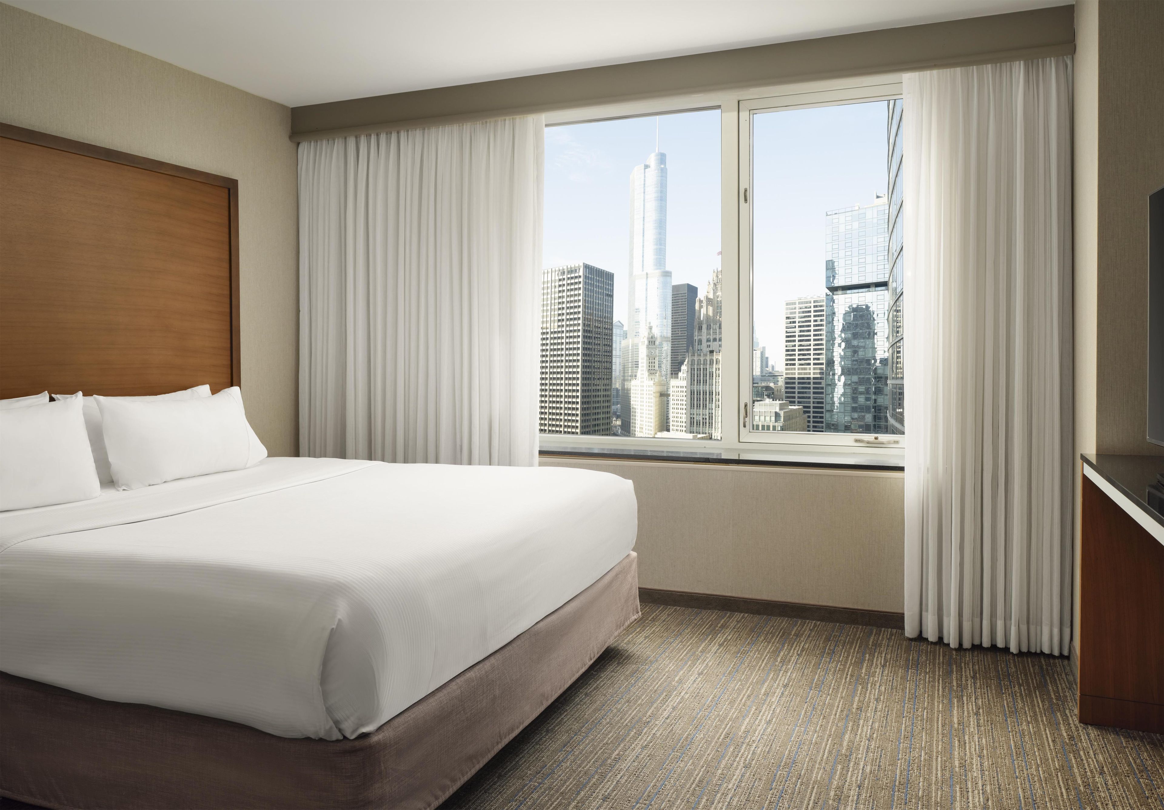 Una habitación de hotel con una cama grande, vistas a la ciudad y un televisor.
