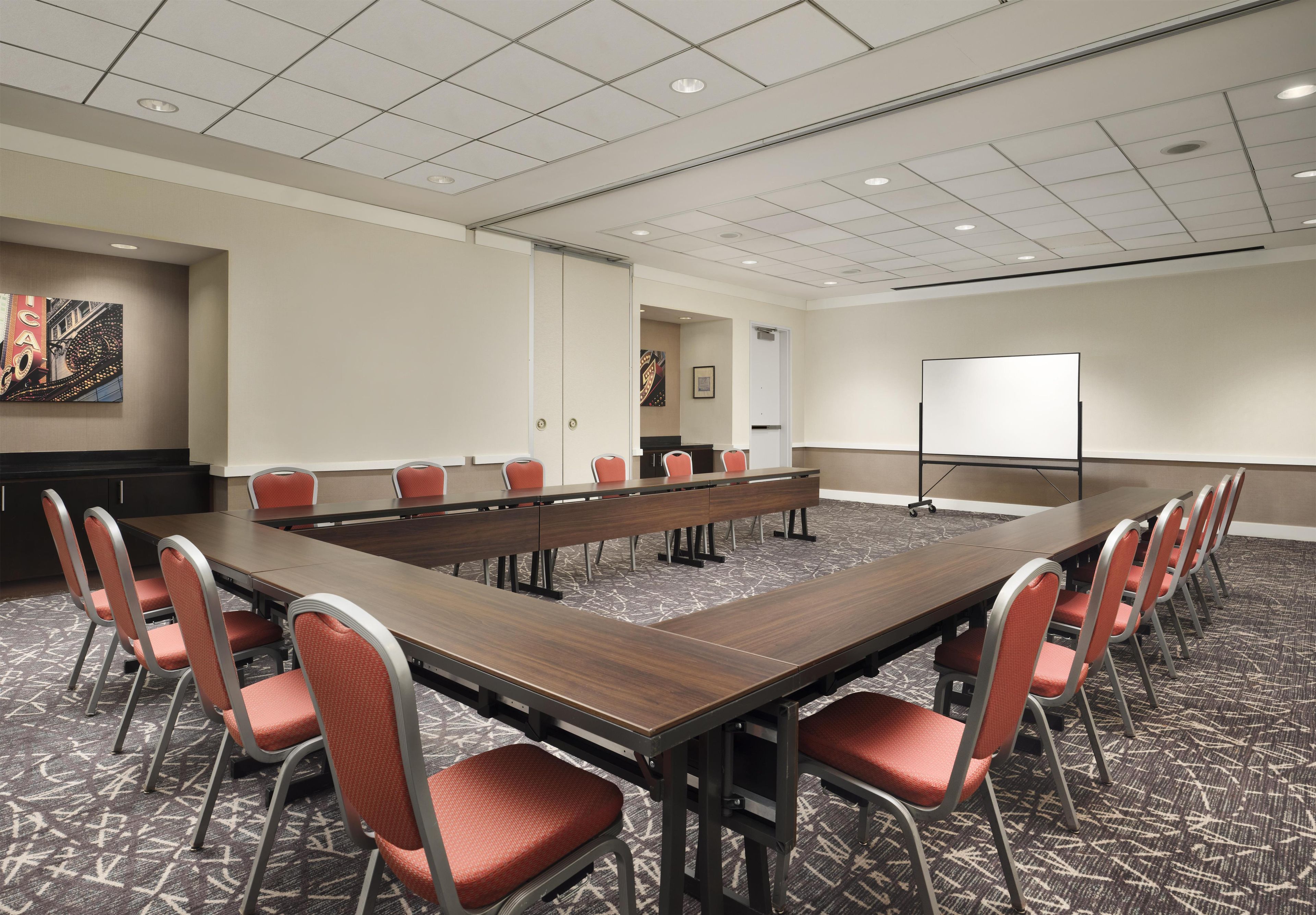 A conference room with a long table, red chairs, a whiteboard, and a carpeted floor.