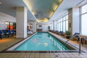 An indoor swimming pool with lounge chairs and tables, a tiled floor, and a ceiling with a unique light fixture. - Embassy Suites by Hilton Chicago Downtown Magnificent Mile (Chicago)