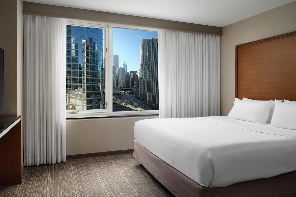 A hotel room with a large bed, a TV, and a window with a city view.
