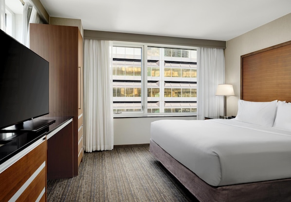 A hotel room with a bed, a TV, a desk, and a window with blinds. - Embassy Suites by Hilton Chicago Downtown Magnificent Mile (Chicago)