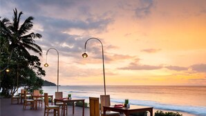 A wooden deck with tables and chairs overlooking the ocean at sunset. - Holiday Resort Lombok (Senggigi)