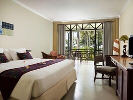 Habitación de hotel con una cama grande, un escritorio, una silla y un balcón con vistas a palmeras.
