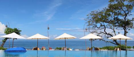 A pool area with umbrellas, lounge chairs, and a view of the sea.