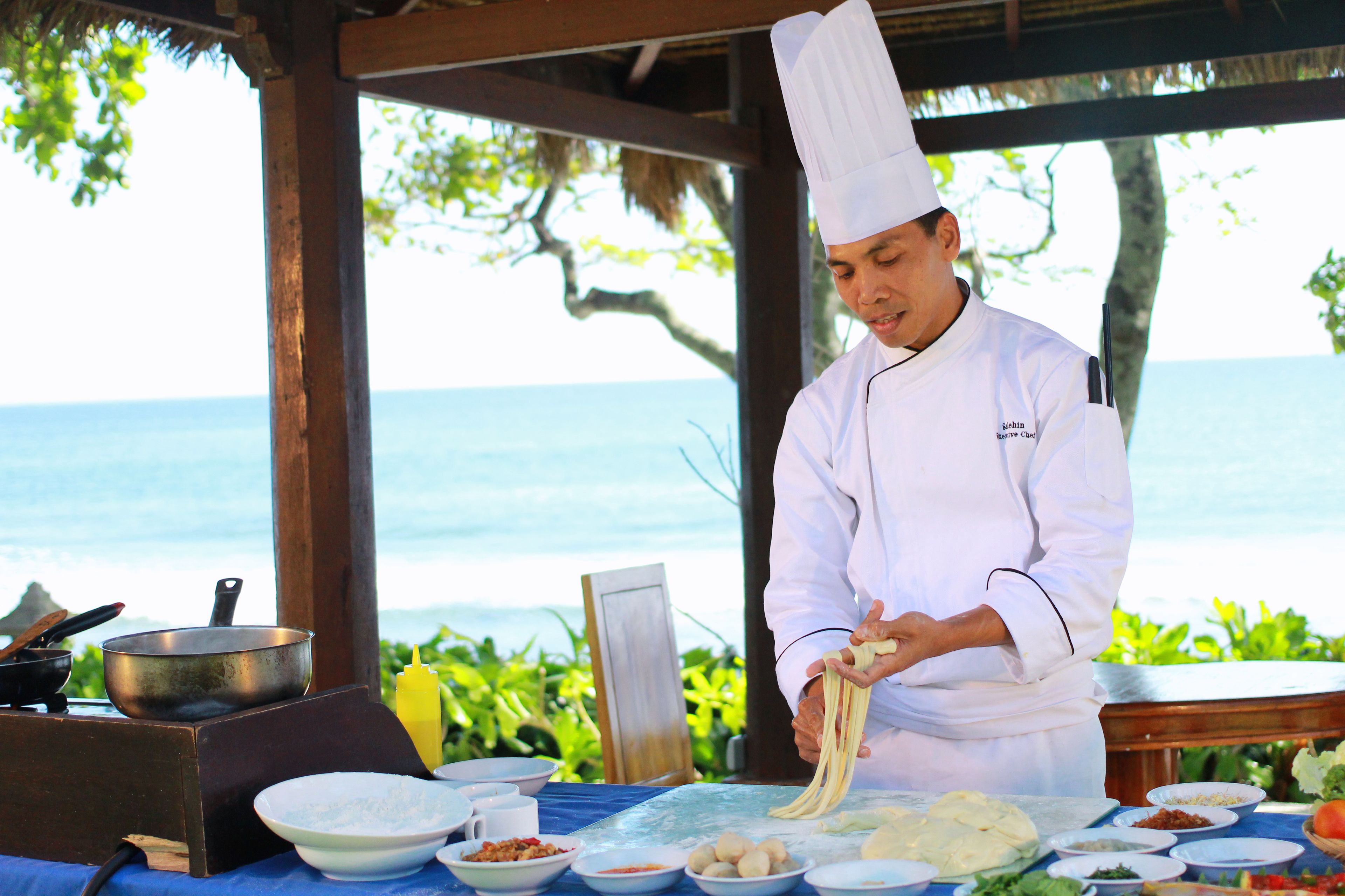 Un chef prepara comida al aire libre con vistas al océano.