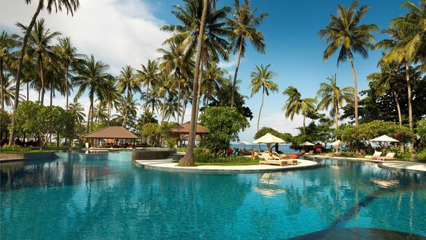 A resort pool with palm trees, lounge chairs, and umbrellas. - Holiday Resort Lombok (Senggigi)