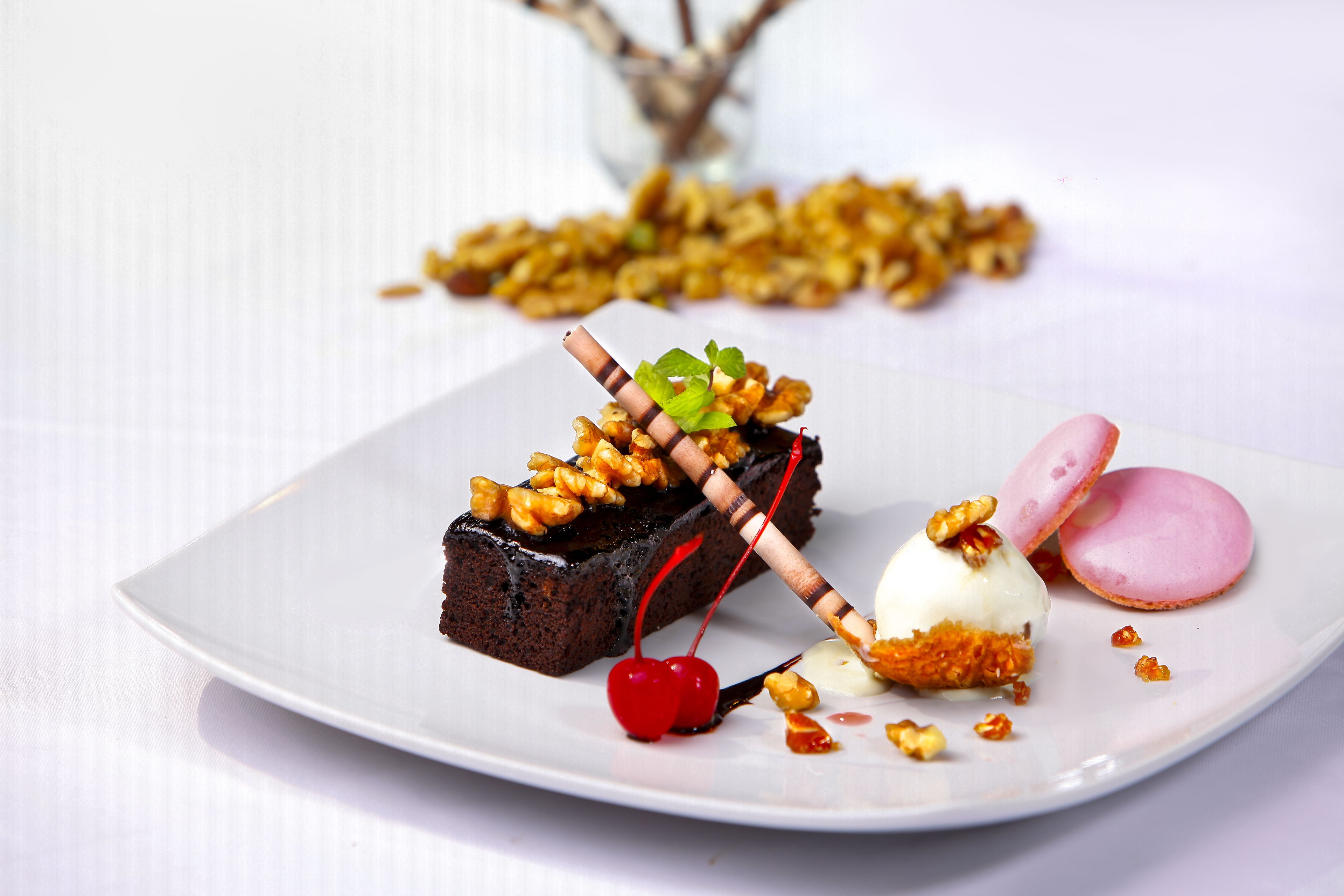 Un plato de postre con pastel de chocolate, cerezas y un macaron rosa.