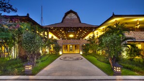 A large, well-lit building with a central entrance, surrounded by lush greenery and stone walls. - Holiday Resort Lombok (Senggigi)