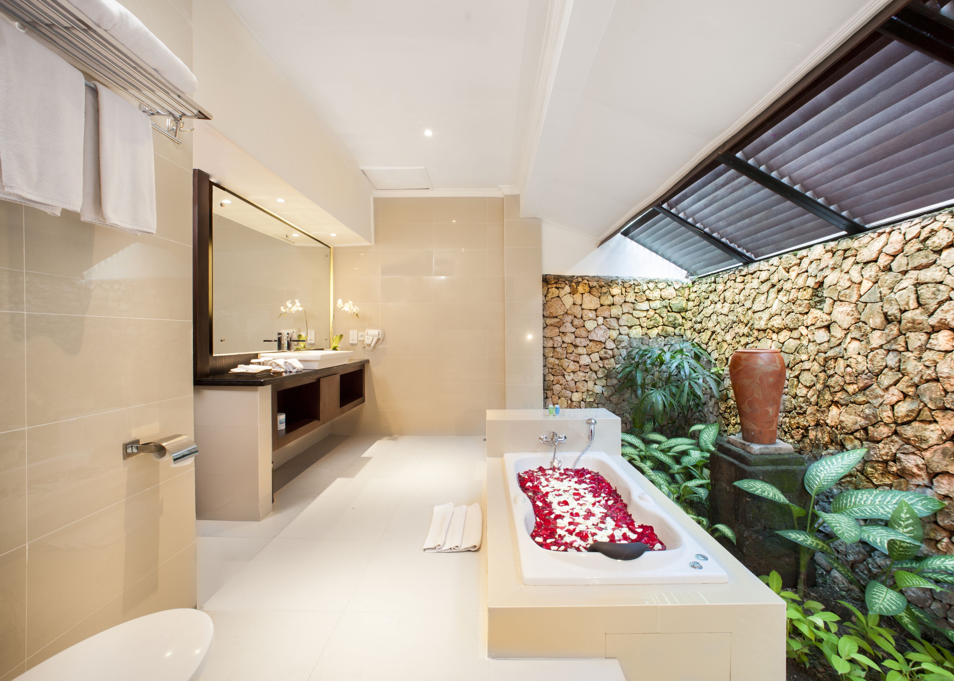 Une salle de bain moderne avec une grande baignoire, un meuble-lavabo avec un miroir et un mur en pierre.