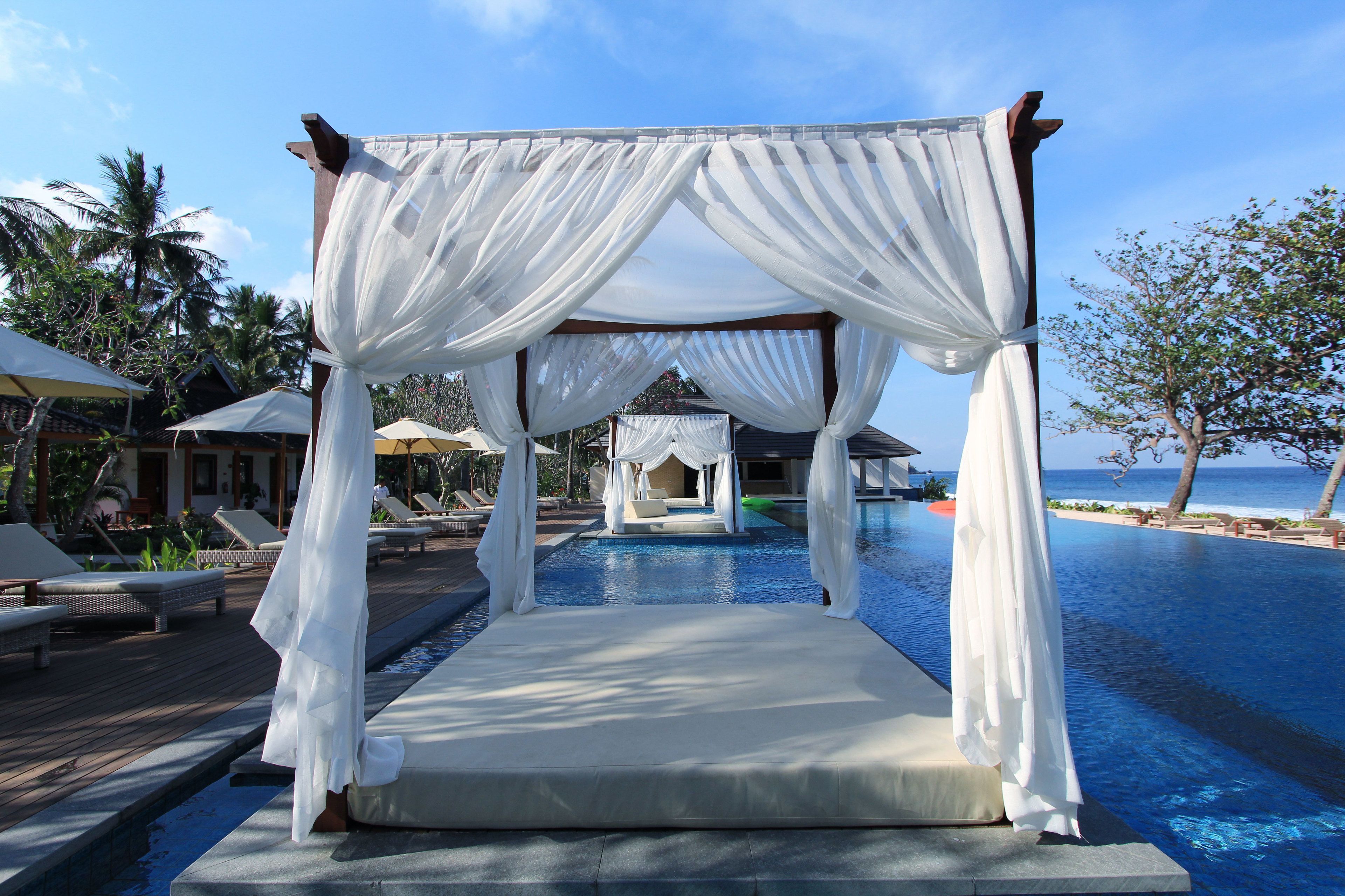 Une tonnelle blanche surplombe un espace piscine aménagé avec des chaises longues et des parasols.