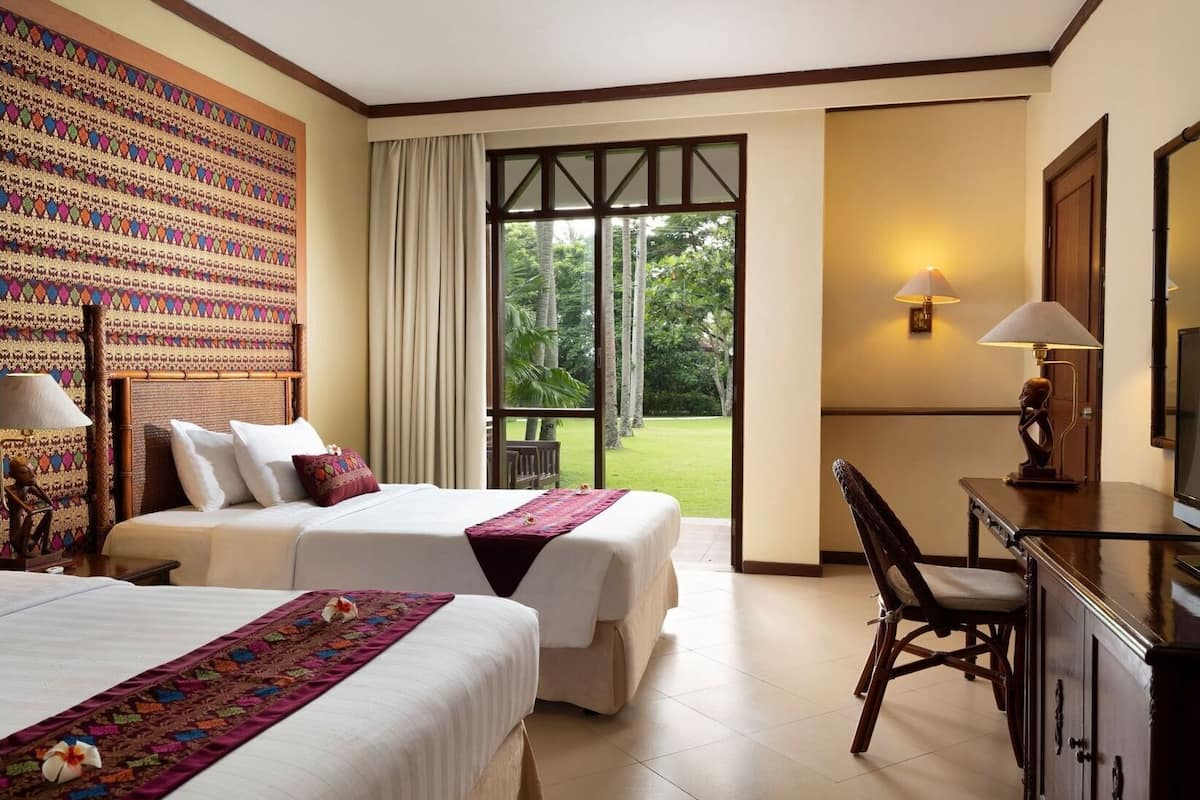 A hotel room with two beds, a desk, a chair, a large window, and a decorative wall.