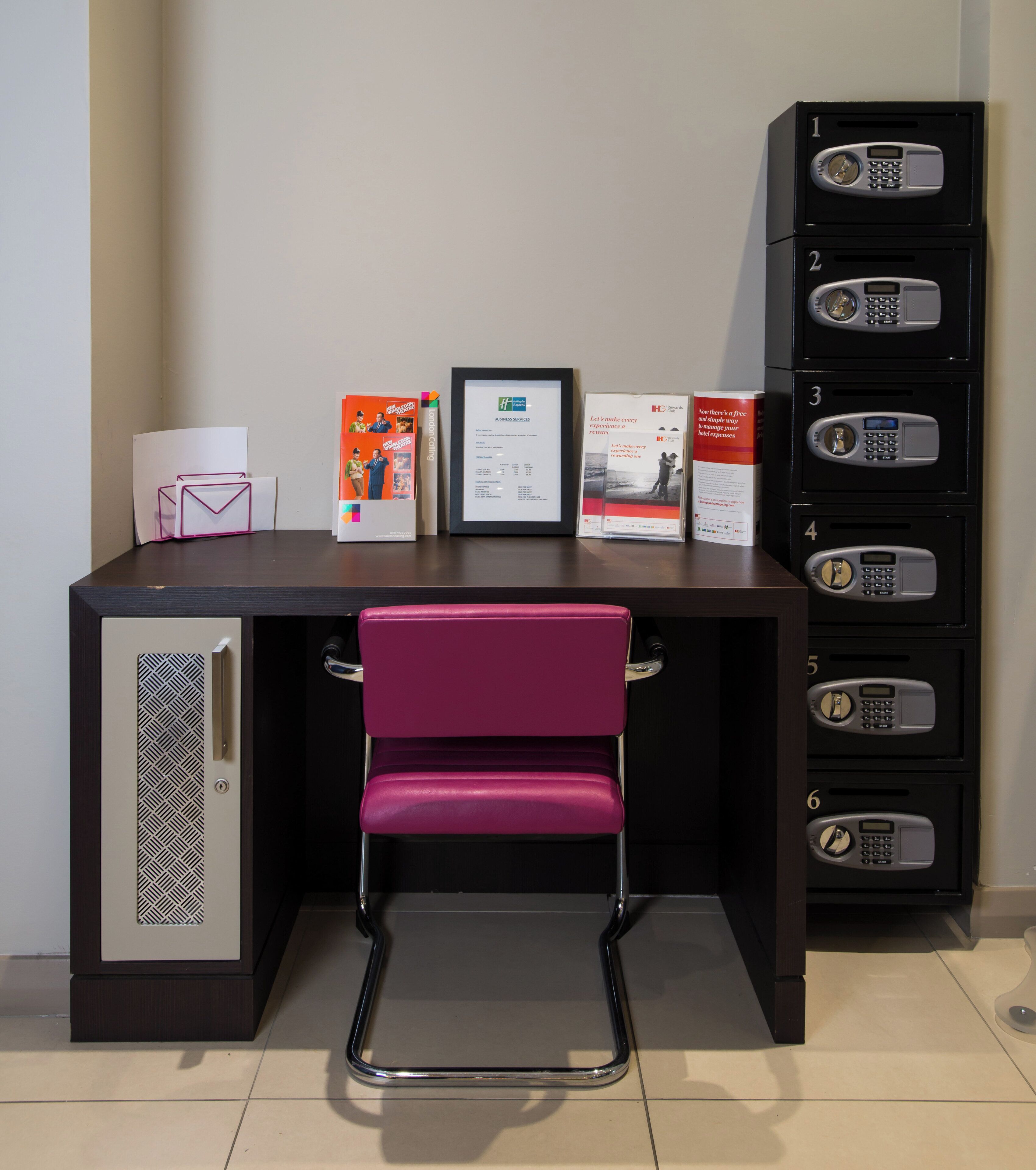 A hotel reception desk with a pink chair, a framed certificate, and informational brochures.