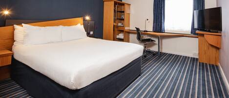 A hotel room with a large bed, a desk, a chair, a television, and a wardrobe.