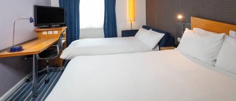 Una habitación de hotel con dos camas, un escritorio, un televisor, una lámpara y una ventana con cortinas.