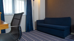A room with a blue sofa, a chair, a lamp, and a window with curtains. - Holiday Inn Express London Wandsworth by IHG (London)