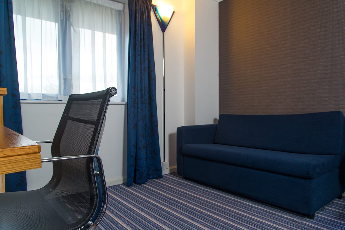 A room with a blue sofa, a chair, a lamp, and a window with curtains.