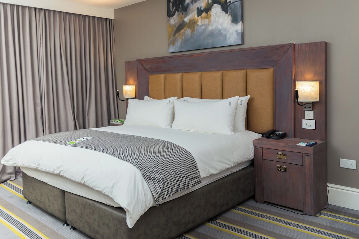Une chambre d’hôtel avec un grand lit, une table de chevet avec un téléphone et un tableau au mur.
