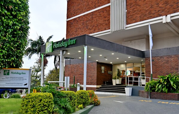A Holiday Inn hotel entrance with a brick facade, covered walkway, and outdoor seating area.