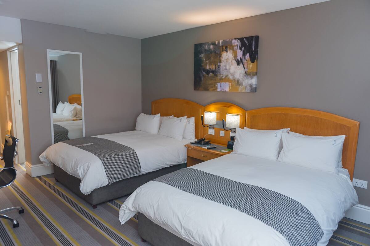 Habitación de hotel con dos camas, un espejo, un cuadro y un escritorio con lámpara.