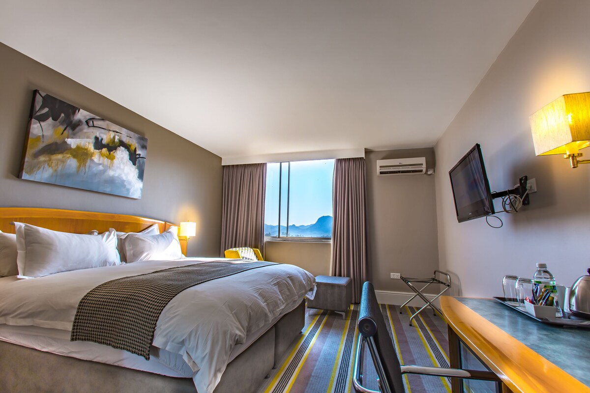 A hotel room with a bed, a desk, a chair, a TV, and a window with curtains.