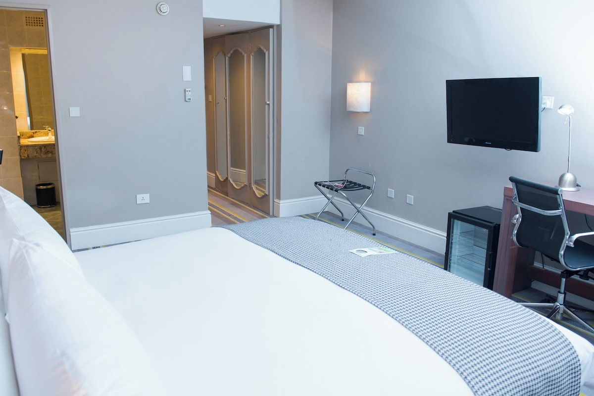 Une chambre d’hôtel avec un lit, un bureau avec un ordinateur, une télévision et un miroir.