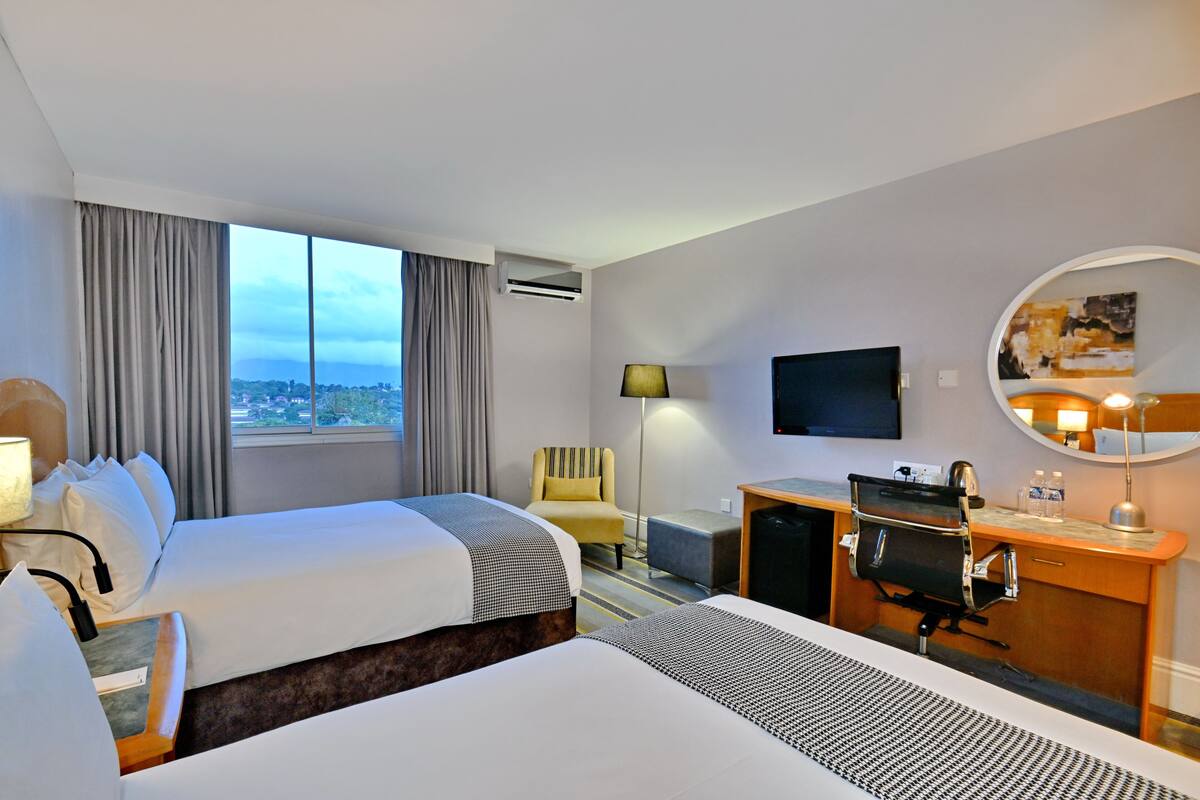 Habitación de hotel con dos camas, un escritorio, una silla, un televisor y una ventana con vistas.