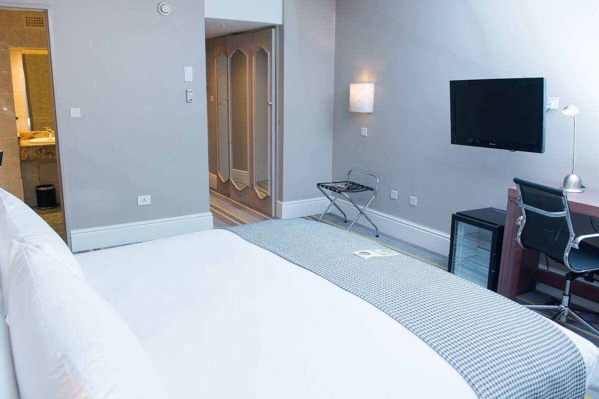 Una habitación de hotel con cama, escritorio, computadora, televisor y espejo.