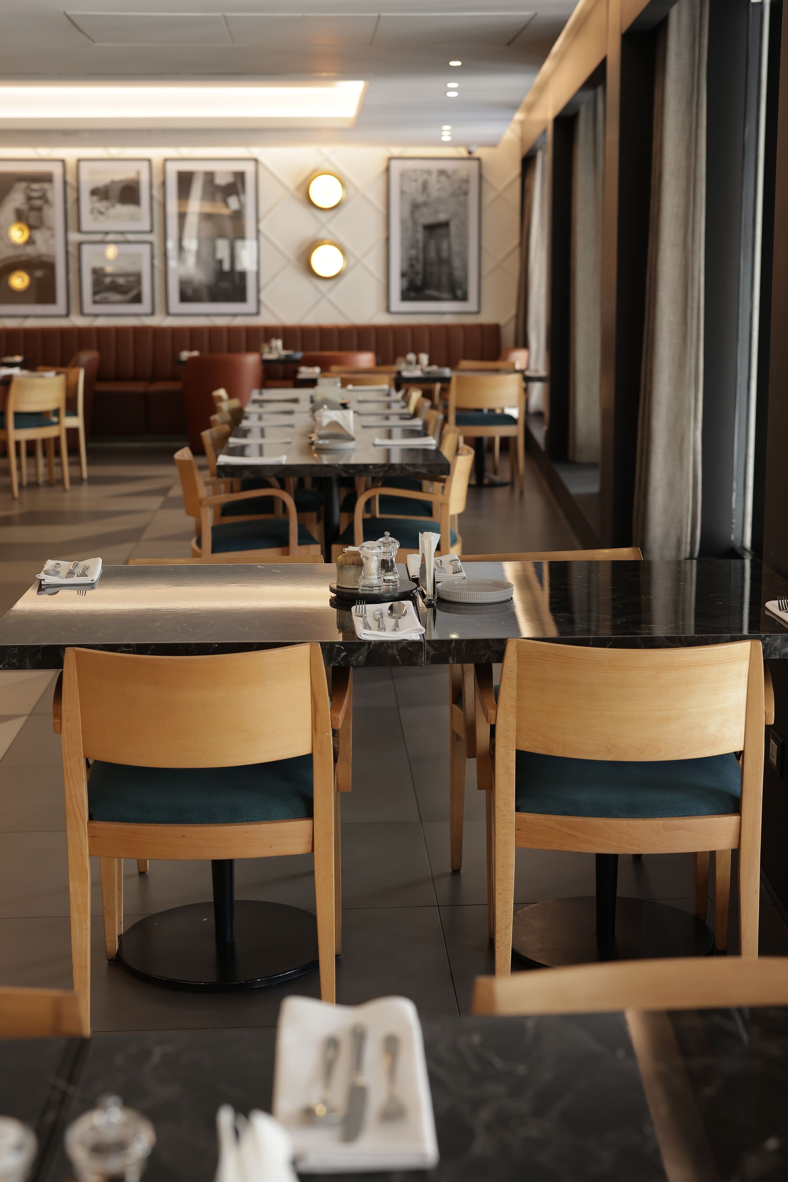 A restaurant with wooden chairs and tables, framed pictures on the wall, and a long counter.