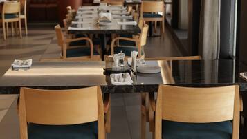 Un restaurante con sillas y mesas de madera, cuadros en la pared y una larga barra.