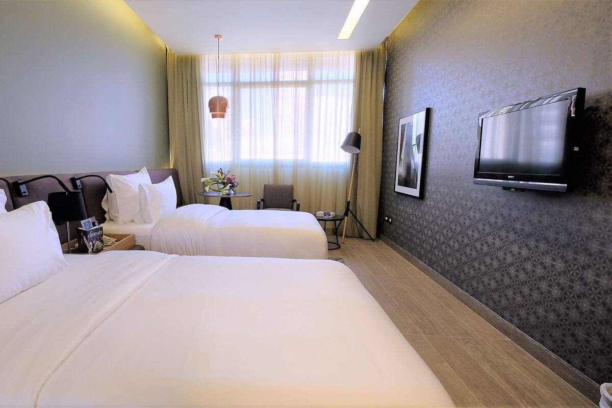 Une chambre d’hôtel avec deux lits, un bureau, une chaise, une télévision et une fenêtre avec des rideaux.