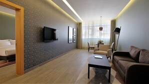 A hotel room with a bed, a TV, a sofa, a coffee table, and a small table with a vase.
