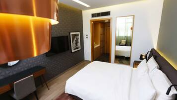A hotel room with a bed, a desk, a TV, a mirror, and a door leading to a bathroom.