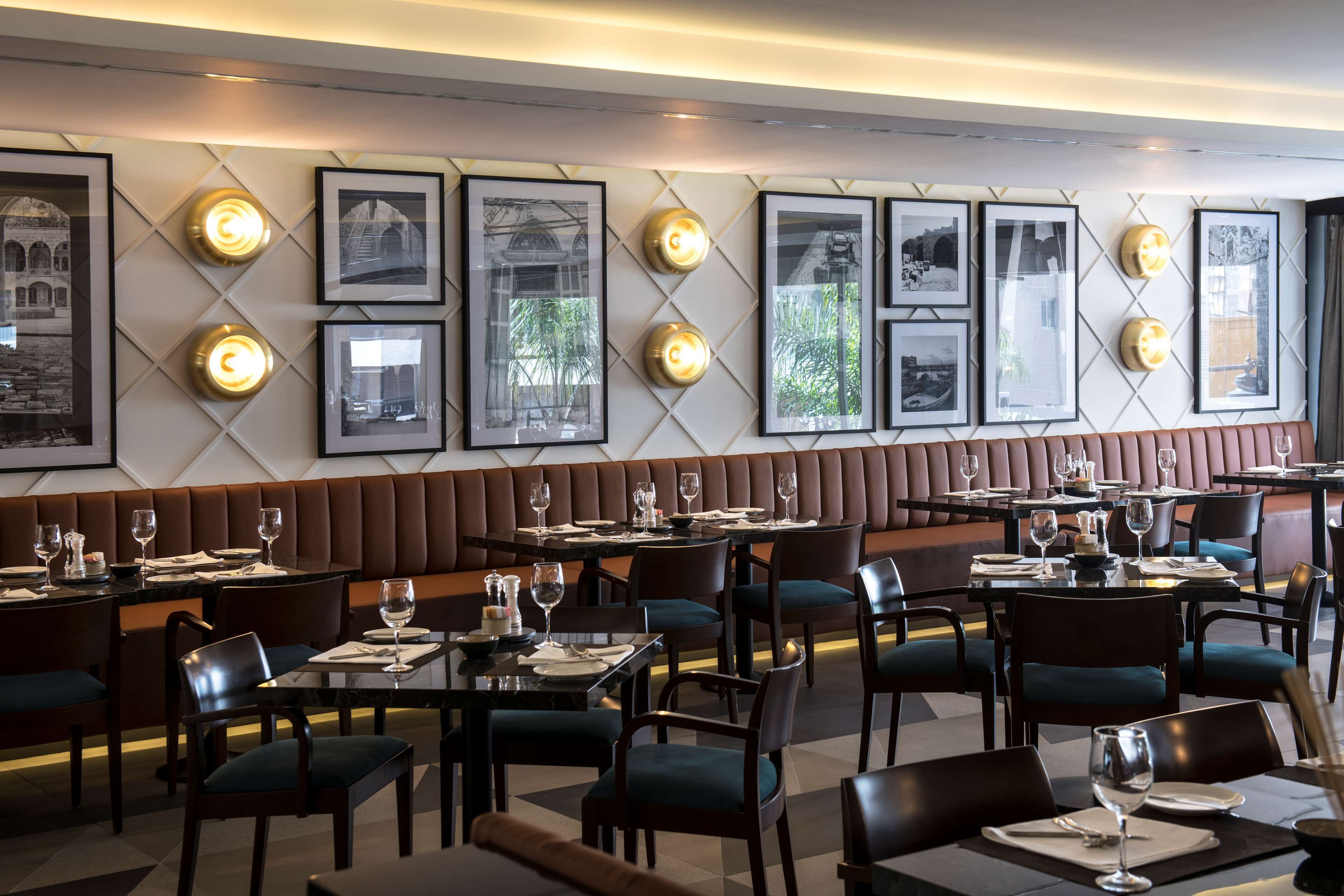 A restaurant with a long bench seating area, tables with chairs, framed pictures on the wall, and a modern interior design.