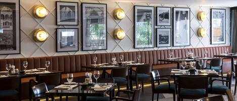 A restaurant with a long bench seating area, tables with chairs, framed pictures on the wall, and a modern interior design.