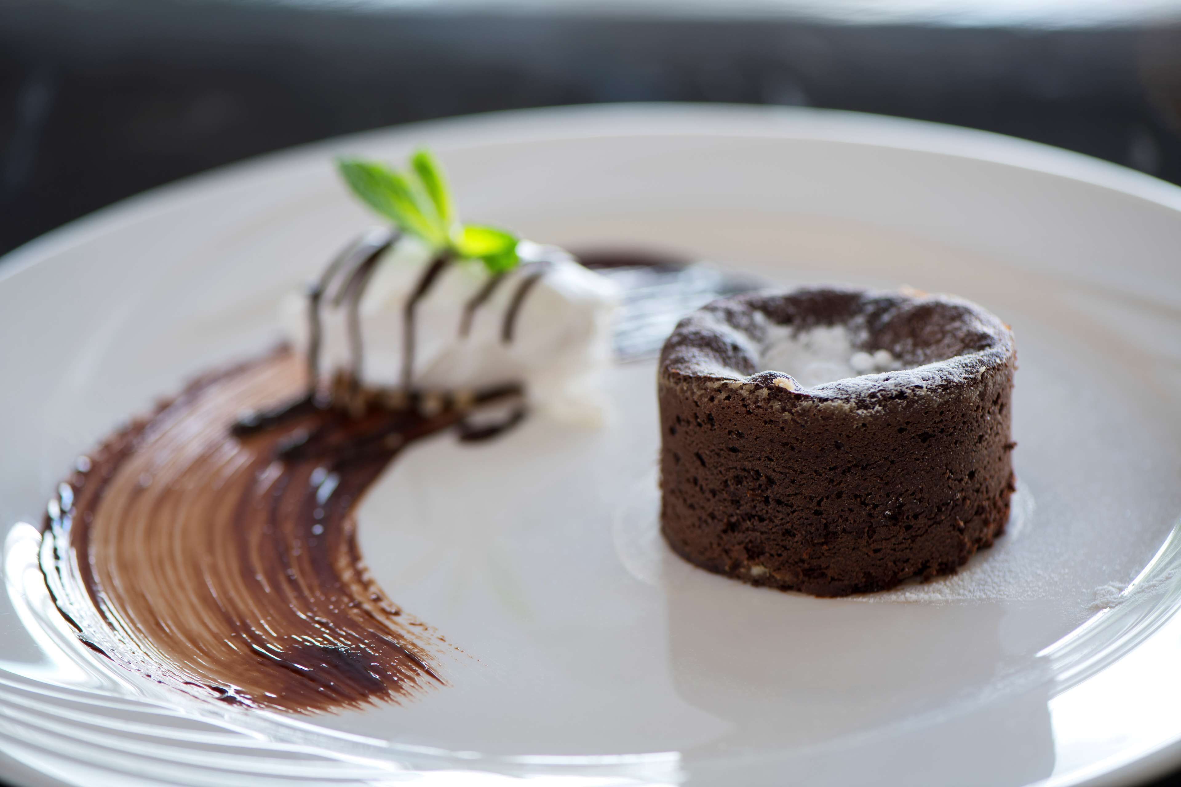 Un postre sobre un plato blanco, con pastel de chocolate y una bola de helado con goteo de chocolate.