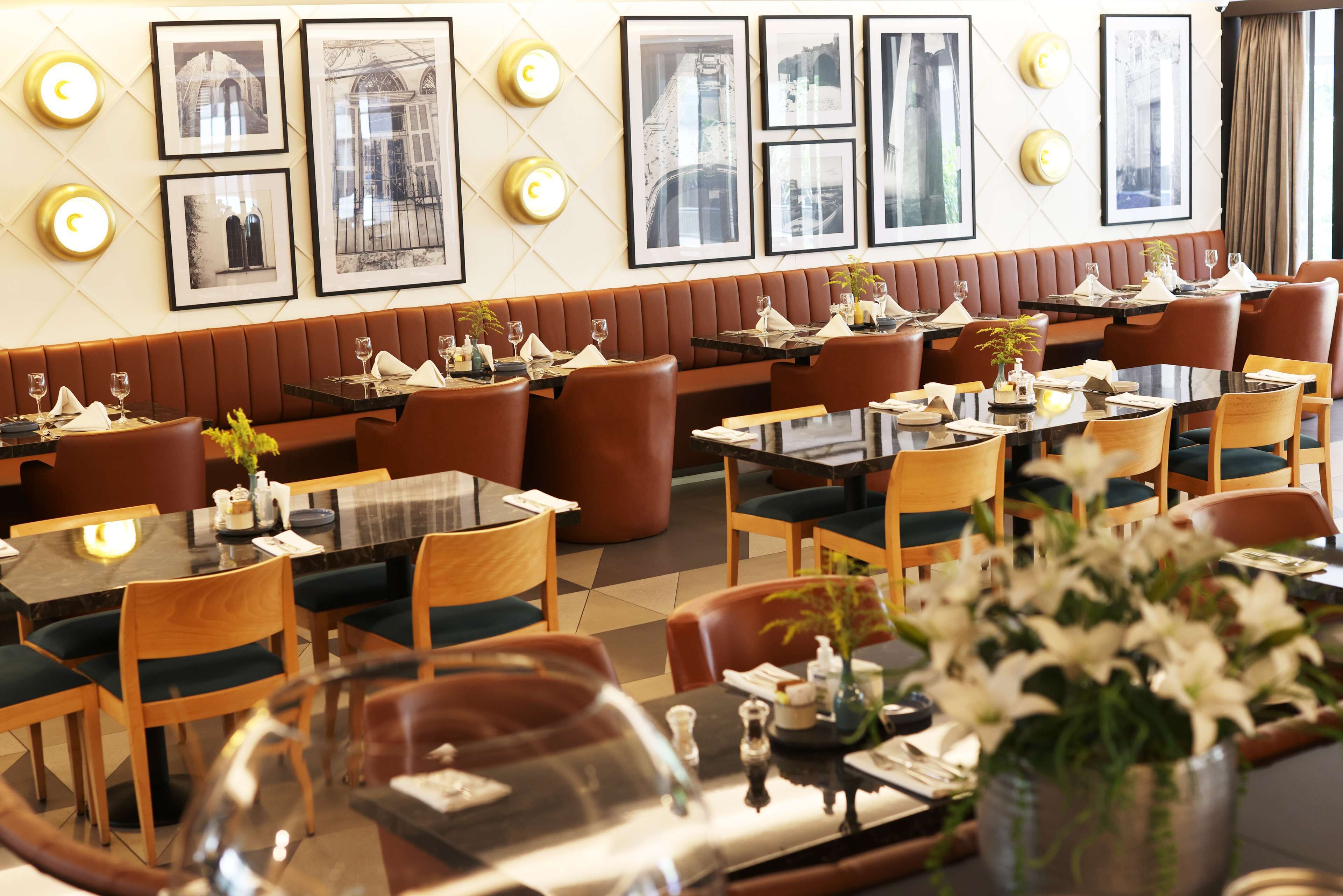 A restaurant with booths and tables, framed pictures on the wall, and a vase of flowers on the table.