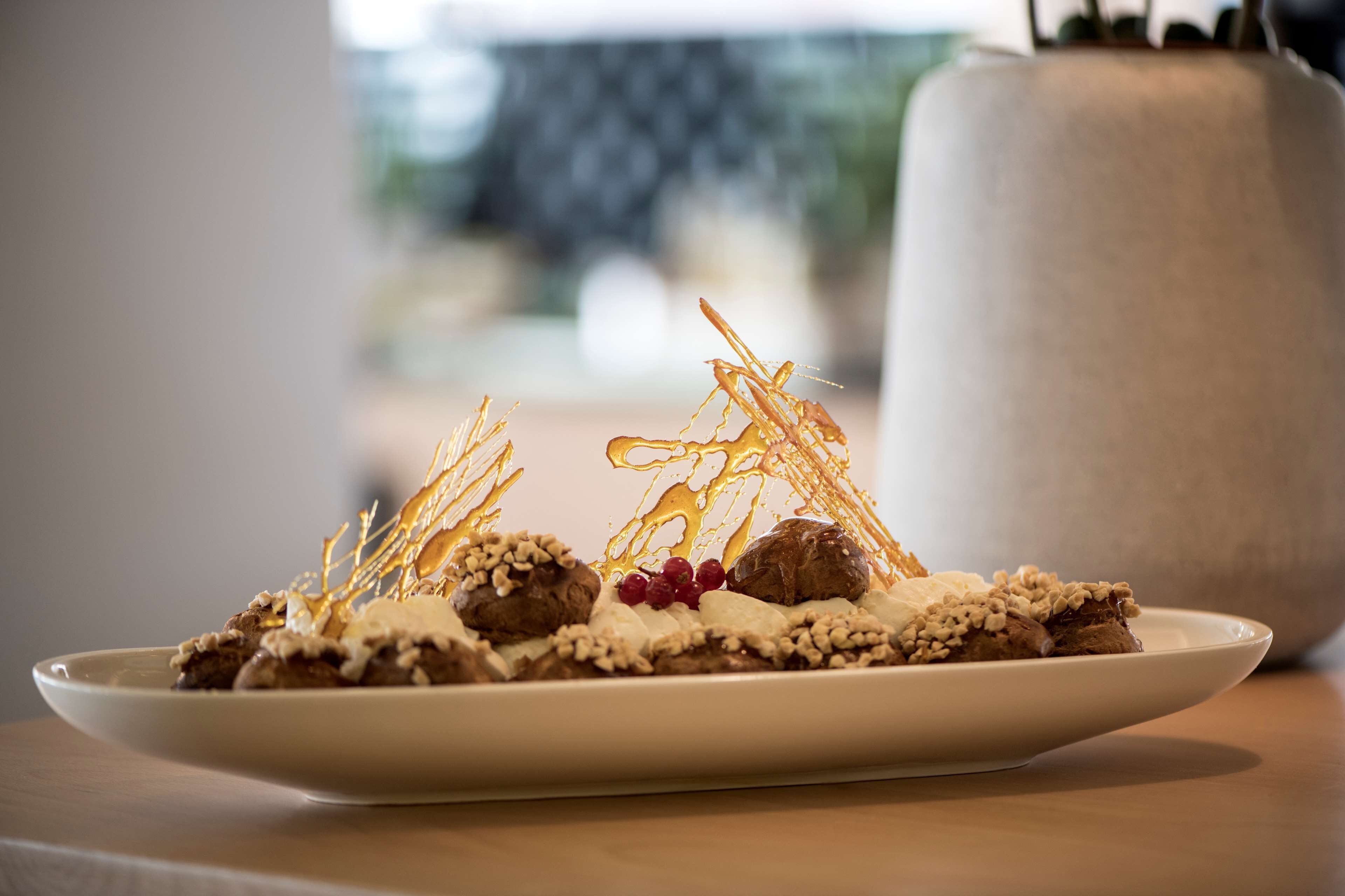 A dessert on a white plate with chocolate pieces, nuts, and berries, with a blurred background.