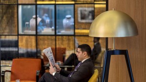 A man seated in a modern hotel lobby with a large lamp, a glass table, and framed pictures on the wall.