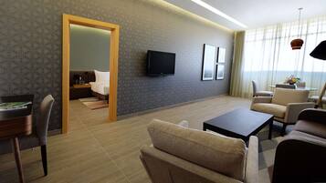 Una habitación de hotel moderna con una puerta de madera que da a un dormitorio, un televisor de pantalla plana en la pared y una zona de estar con una mesa de café y sillas.