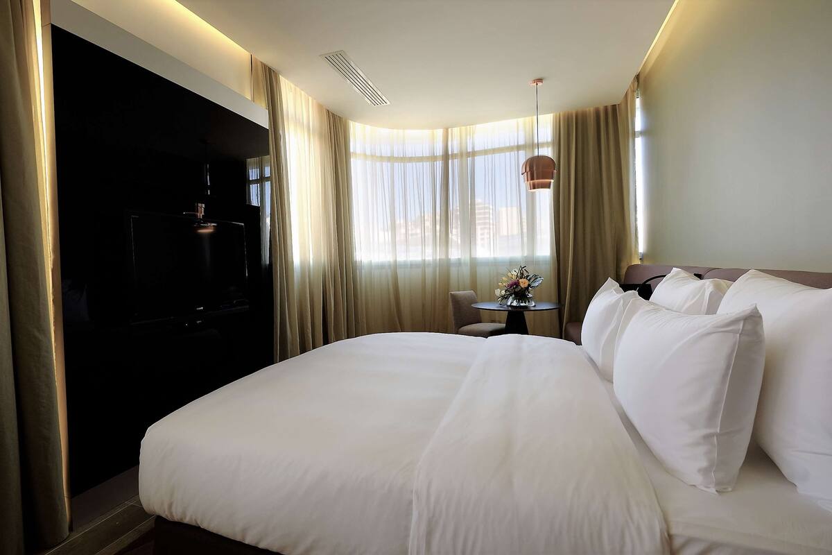 Une chambre d’hôtel avec un grand lit, une petite table sur laquelle se trouve un vase, et un téléviseur posé sur un meuble.