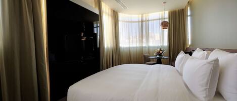 Una habitación de hotel con una cama grande, una mesita con un florero y un televisor sobre un mueble.