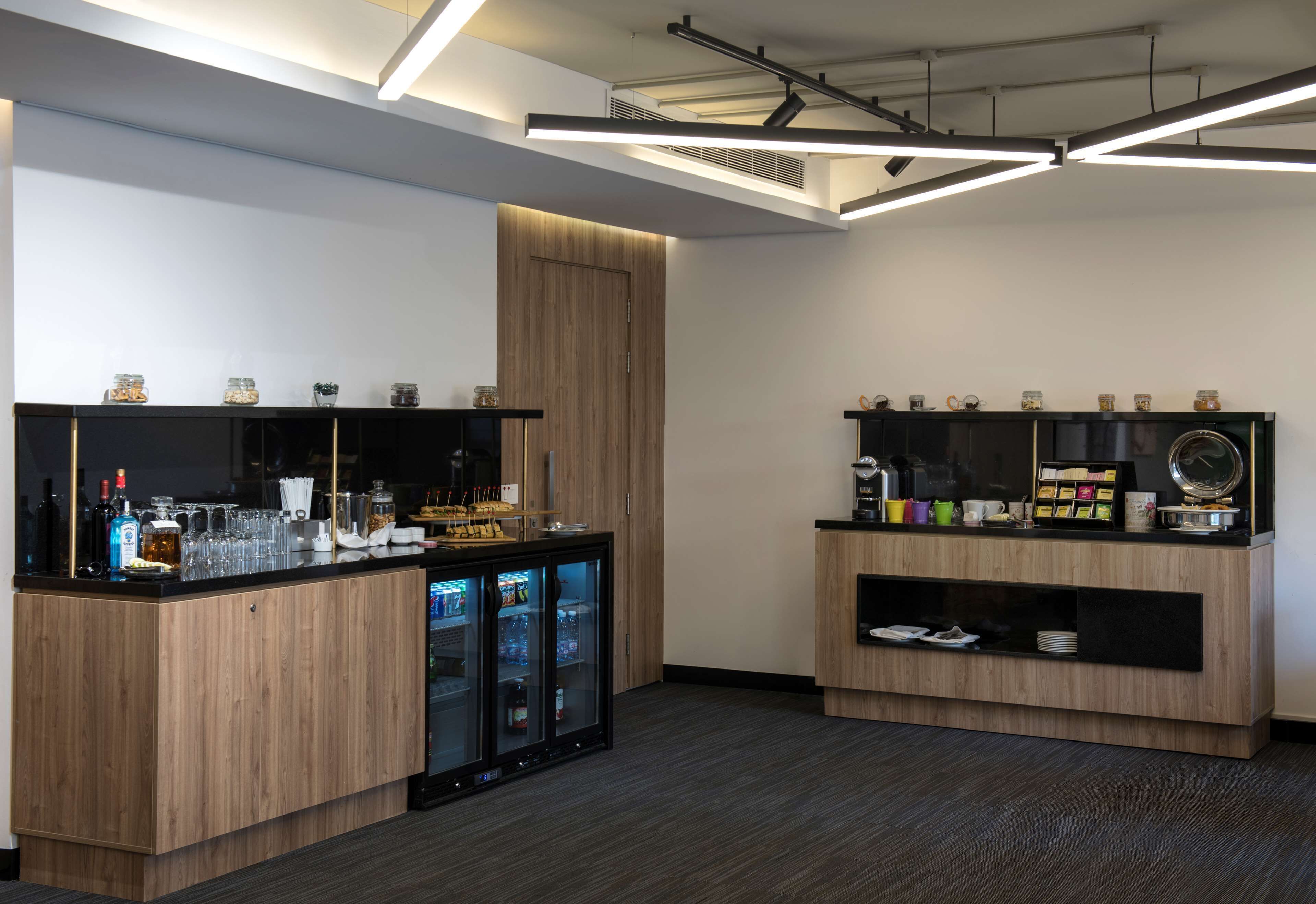 Zona de bar moderna con armarios de madera, mostrador refrigerado y distintos utensilios de bar.