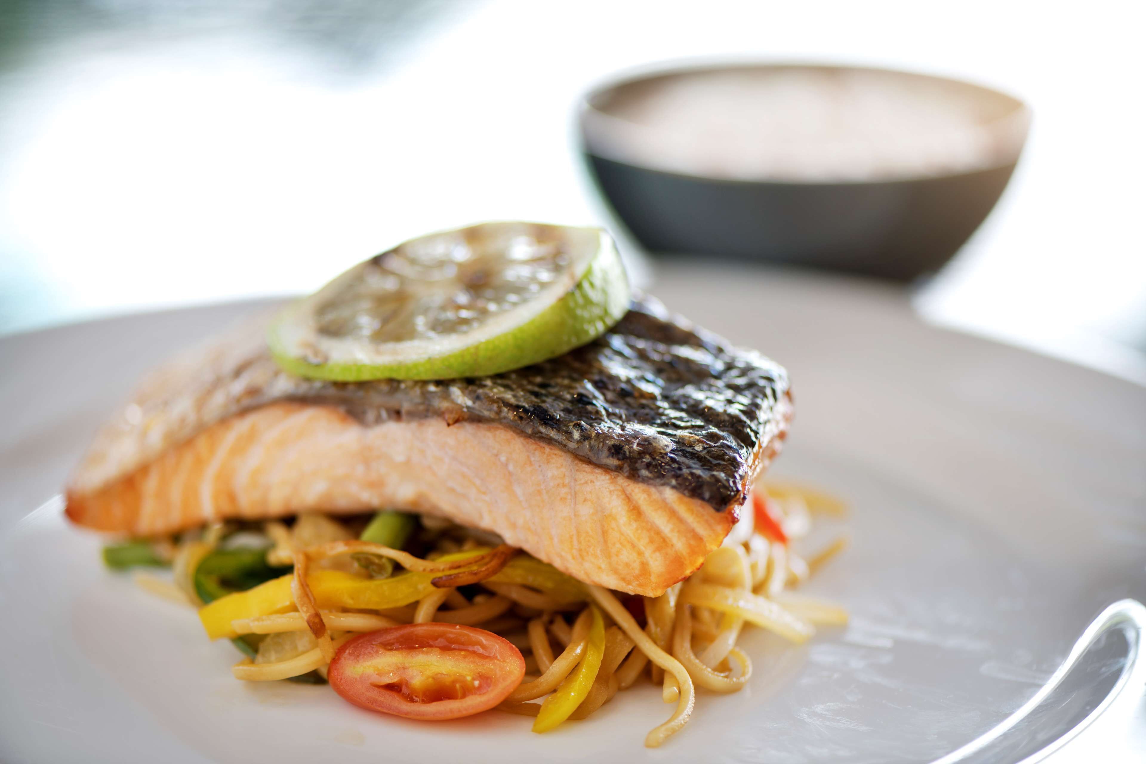 A plate with a piece of salmon, noodles, and a slice of lime.