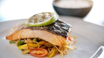 A plate with a piece of salmon, noodles, and a slice of lime.