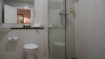 A modern bathroom with a glass-enclosed shower, a white toilet, and a sink with toiletries.