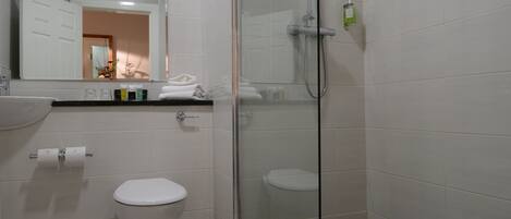 A modern bathroom with a glass-enclosed shower, a white toilet, and a sink with toiletries.