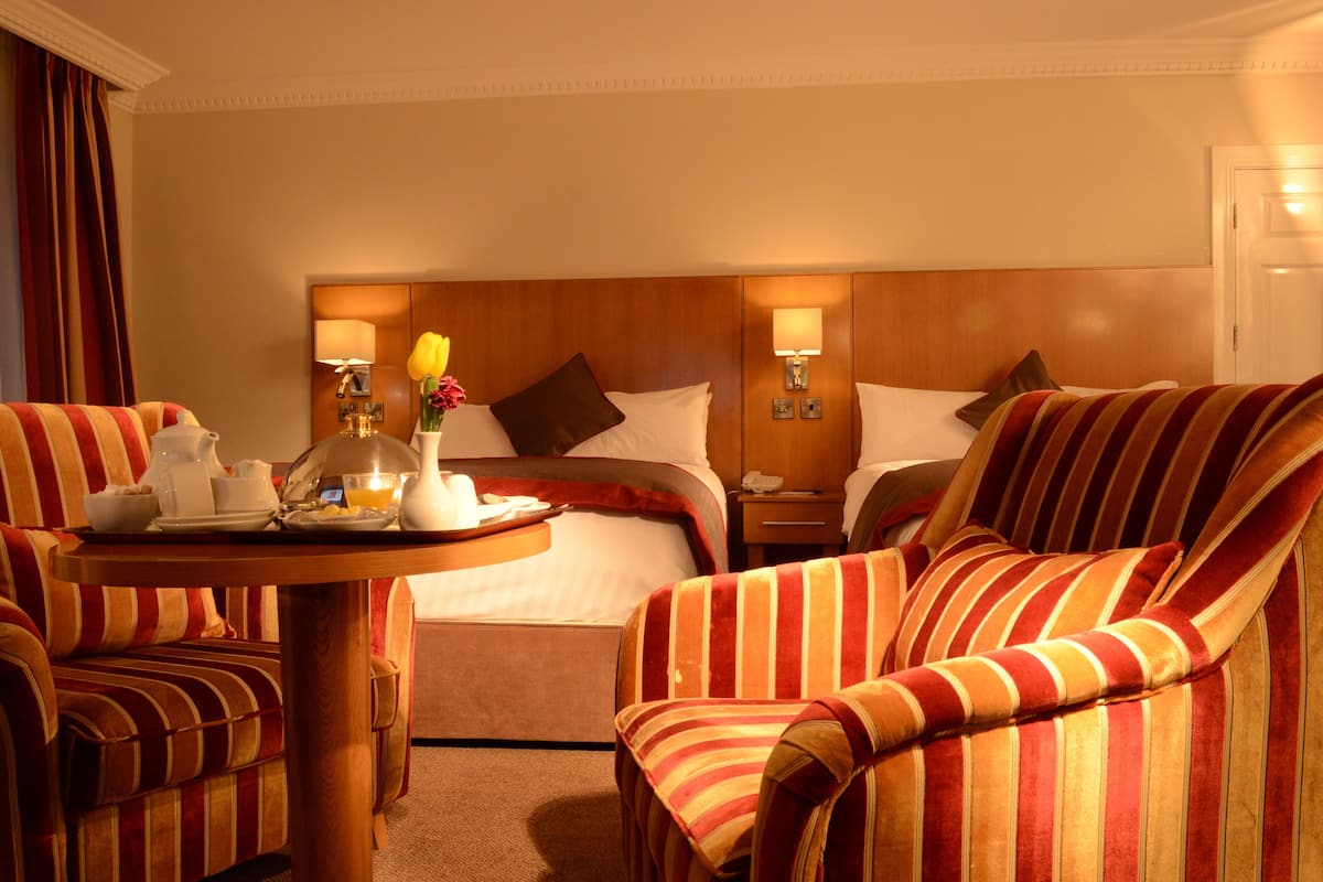 Habitación de hotel con cama, dos sillones a rayas, una mesita con alimentos para el desayuno y lámparas de noche.