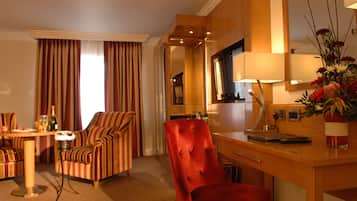 Habitación de hotel con comedor, un sillón rojo, un sofá, un escritorio de madera, un espejo y un jarrón con flores.