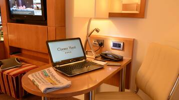 Habitación de hotel con una computadora portátil sobre un escritorio de madera, un periódico, un teléfono y un televisor montado en la pared.